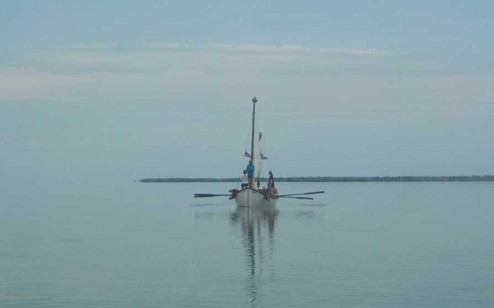A sailboat floats in calm water. Fog appears to be rolling in or out. 